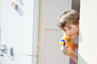 Boy holding water pistol and peering out of caravan, portrait - ISF19313