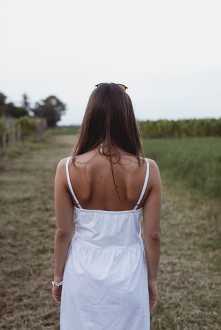 Frau im weißen Sommerkleid, Spaziergang im Weinberg, Rückansicht, lizenzfreies Stockfoto