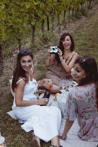 Freunde machen ein Picknick in einem Weinberg, eine Frau fotografiert mit einer Sofortbildkamera, lizenzfreies Stockfoto