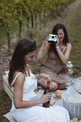 Freunde machen ein Picknick in einem Weinberg, eine Frau fotografiert mit einer Sofortbildkamera - MAUF01624
