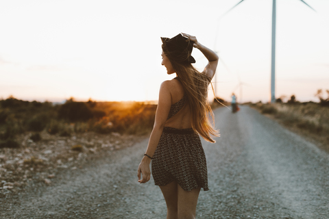 Rückenansicht einer jungen Frau, die in der Abenddämmerung auf einer Landstraße geht, lizenzfreies Stockfoto