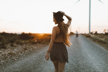 Back view of young woman walking on rural road at evening twilight - OCAF00340