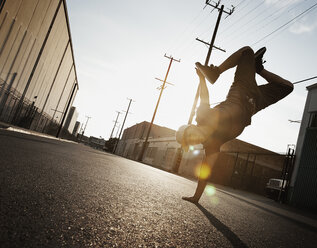 Ein junger Mann tanzt Breakdance auf der Straße einer Stadt und macht einen einhändigen Handstand. - MINF03114