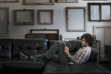 Loft decor. A wall hung with blank canvases. A man on a sofa using a digital tablet. - MINF03131