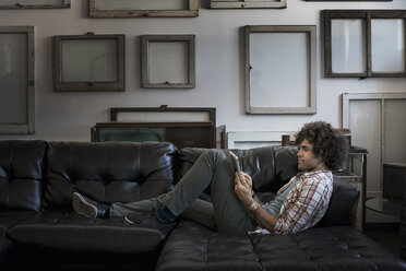 Loft-Dekor. Eine Wand mit leeren Leinwänden. Ein Mann auf einem Sofa, der ein digitales Tablet benutzt. - MINF03131