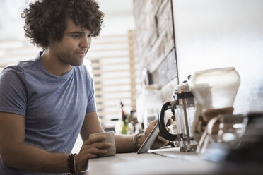 Loft living. A young man sitting with a cup of coffee, holding a digital tablet. - MINF03143