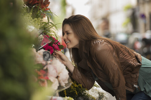 Eine Frau beugt sich vor, um den Duft der Blumen an einem Stand auf der Straße zu riechen. - MINF03149