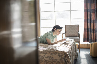 Eine junge Frau liegt auf einem Bett in einem Motelzimmer und benutzt einen digitalen Touchscreen. - MINF03156