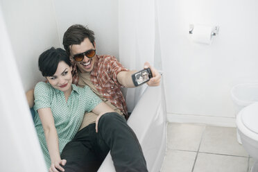 Ein junges Paar sitzt vollständig bekleidet in einer Badewanne im Badezimmer und macht ein Selfie. - MINF03165