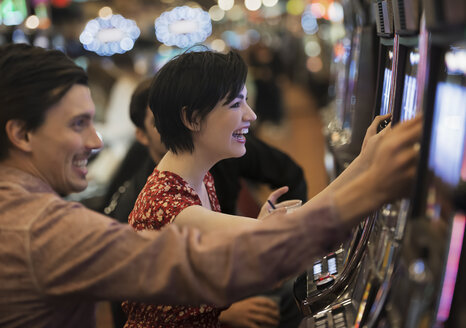 Zwei Personen, ein junger Mann und eine Frau, spielen in einem Kasino an den Spielautomaten. - MINF03170