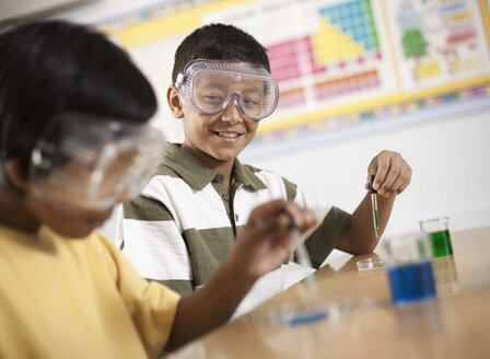 Zwei junge Menschen, ein Junge und ein Mädchen, die im naturwissenschaftlichen Unterricht mit Schutzbrillen an einem Experiment arbeiten. - MINF03184