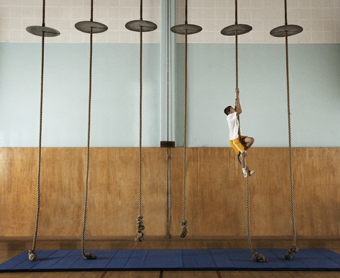 Ein Kind klettert in der Turnhalle einer Schule an einem Seil hoch., lizenzfreies Stockfoto