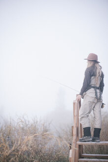 Eine Frau steht auf einem hölzernen Stil im Nebel. - MINF03188