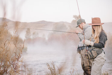 A couple fishing on a riverbank, tying the flies to the hooks for fly-fishing. - MINF03191