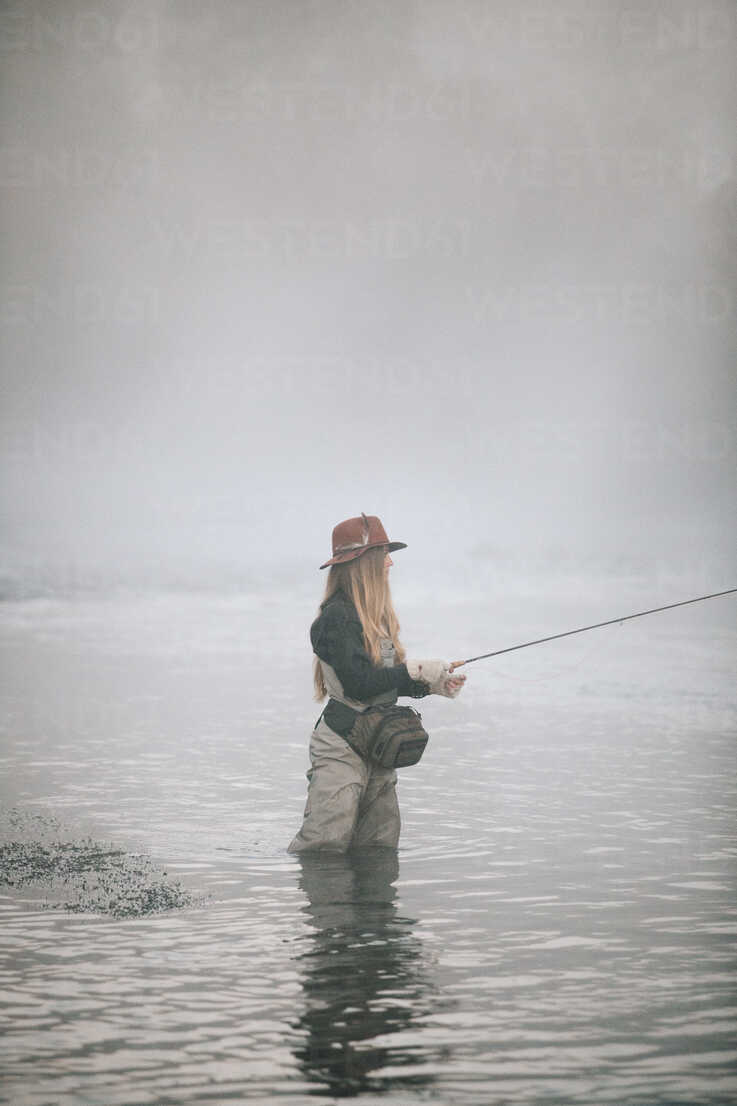 A woman fisherman fly-fishing, standing in waders in thigh deep