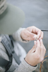 A person's hands tying a fishing fly onto a hook. - MINF03196