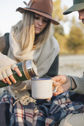 A woman pouring a hot drink from a vacuum flask into a cup on a winter picnic. - MINF03199