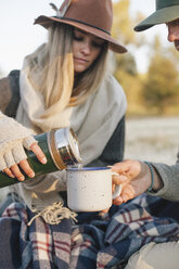 Eine Frau gießt bei einem Winterpicknick ein heißes Getränk aus einer Isolierflasche in eine Tasse. - MINF03199