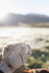 A person wearing mittens holding a hot drink in her hands. - MINF03201