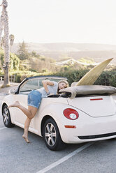 Eine junge Frau in Demin-Shorts lehnt sich in ein Cabrio mit einem Surfbrett auf dem Rücksitz. - MINF03226
