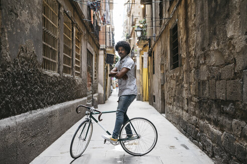 Spain, Barcelona, man standing with racing cycle in an alley - JRFF01733