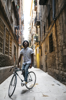 Spain, Barcelona, man standing with racing cycle in an alley looking up - JRFF01734