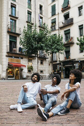 Spanien, Barcelona, drei Freunde sitzen auf einem Platz und schauen nach oben - JRFF01736