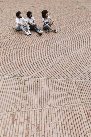 Drei Freunde sitzen auf einem Platz und beobachten etwas, lizenzfreies Stockfoto