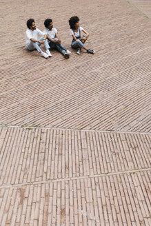 Three friends sitting on a square watching something - JRFF01737