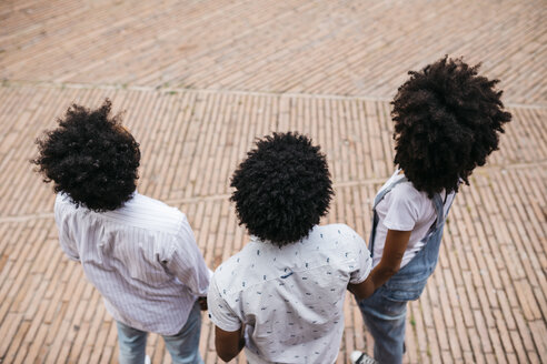 Rückenansicht von drei Freunden mit lockigem Haar, die auf einem Platz stehen - JRFF01740