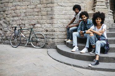 Gruppe von drei Freunden sitzt zusammen auf einer Treppe in der Stadt - JRFF01743