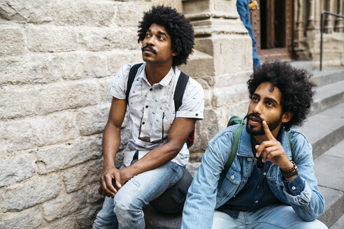 Portrait of two men sitting together on stairs watching something - JRFF01744