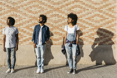 Three friends standing in front of a brick wall sunbathing - JRFF01745