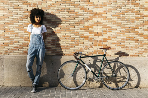 Woman with racing cycle leaning against brick wall - JRFF01747