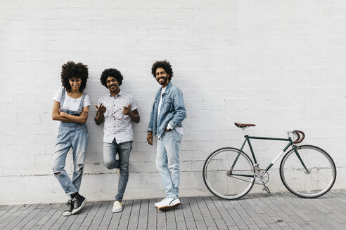 Group of three friends with racing cycle leaning against wall - JRFF01749