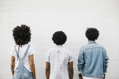 Rückenansicht von drei Freundinnen mit lockigem Haar vor einer weißen Wand - JRFF01752