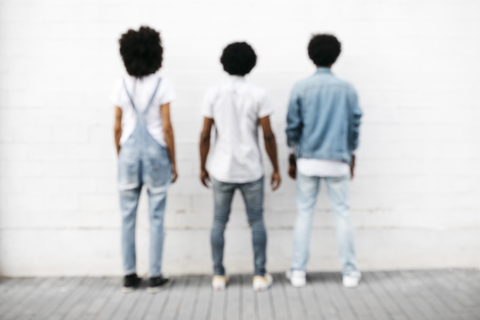 Rückenansicht von drei Freunden, die nebeneinander vor einer weißen Wand stehen, lizenzfreies Stockfoto
