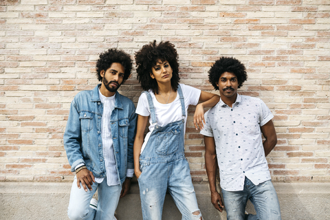 Porträt von drei Freunden in Jeans, die vor einer Backsteinmauer stehen, lizenzfreies Stockfoto