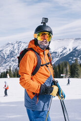 Ein Mann in orangefarbener Skijacke, mit einer Kopfkamera und einem Helm. - MINF03326