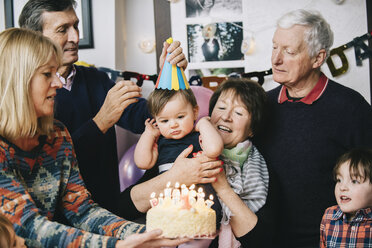 A family gathered to celebrate a one year old girl's birthday party. A cake with lots of candles. - MINF03334