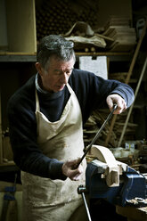 Ein Mann arbeitet in der Werkstatt eines Möbelbauers mit einer Raspel an einer Holzform in einer Klemme. - MINF03338