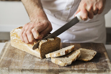 Close up of a baker slicing a freshly baked loaf of bread with a bread knife. - MINF03361