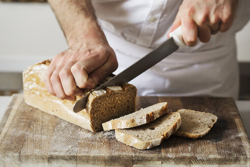 Nahaufnahme eines Bäckers, der einen frisch gebackenen Laib Brot mit einem Brotmesser schneidet. - MINF03361