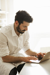 Baker wearing an apron sitting at a laptop computer, typing. - MINF03368