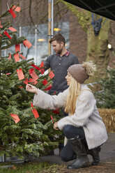 Eine Frau, die einen traditionellen Tannenbaum auswählt, betrachtet die roten handgeschriebenen Etiketten auf einer Tanne. - MINF03395