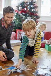 Ein Mann und zwei Kinder finden und packen am Weihnachtstag Geschenke aus. - MINF03408