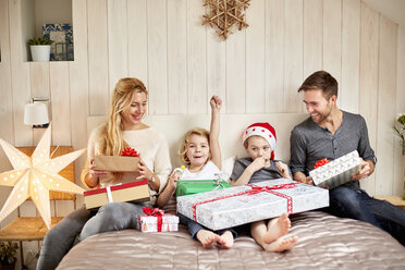 Eine Familie, zwei Erwachsene und zwei Kinder, die am Weihnachtsmorgen im Bett sitzen und gemeinsam die Geschenke öffnen. - MINF03414