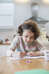 A girl sitting at a kitchen table writing a card or letter. - MINF03420