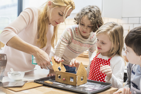 Eine Frau und drei Kinder beim Backen eines Lebkuchenhauses., lizenzfreies Stockfoto