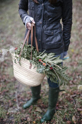 Eine Frau trägt einen Korb mit Laub, immergrünen Zweigen und glänzendem Lorbeer mit Beeren. - MINF03425